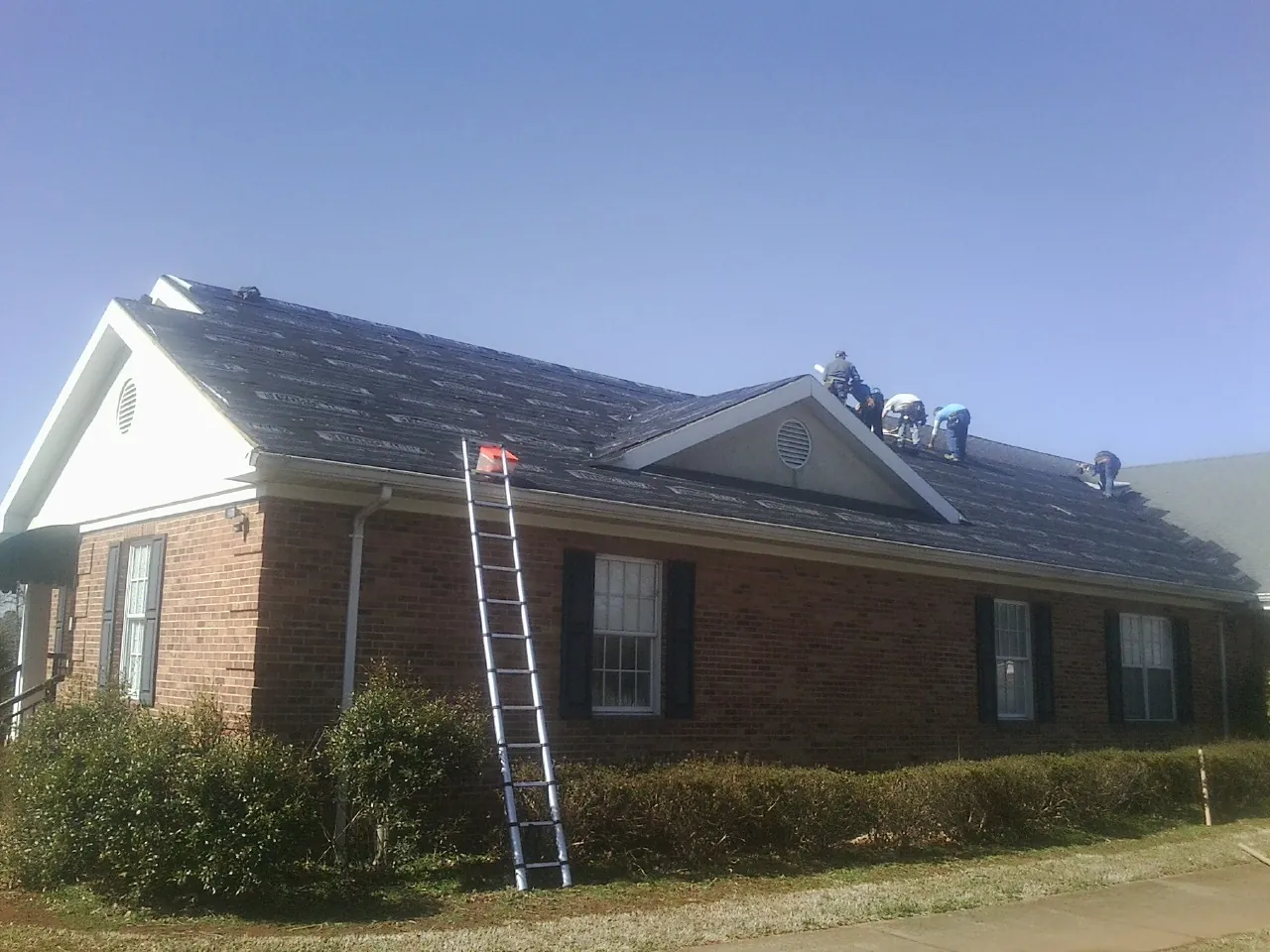 Crew tearing shingles off a brick ranch roof with a ladder set — Metal Roof Repair work by our crew in Martinsburg