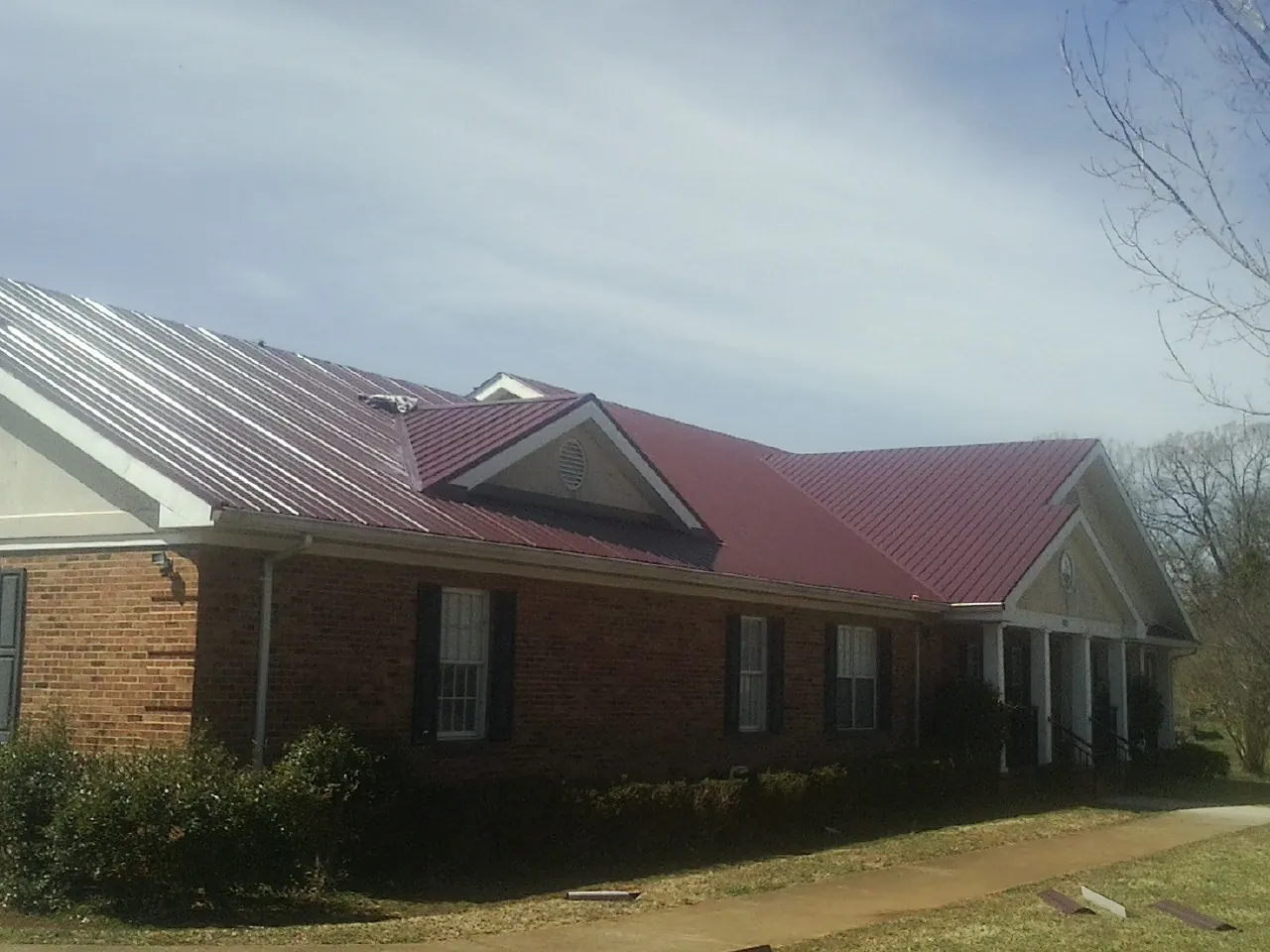 Red metal roof with gabled entries on a long brick building, from a Hail Damage Roof Repair job in Martinsburg
